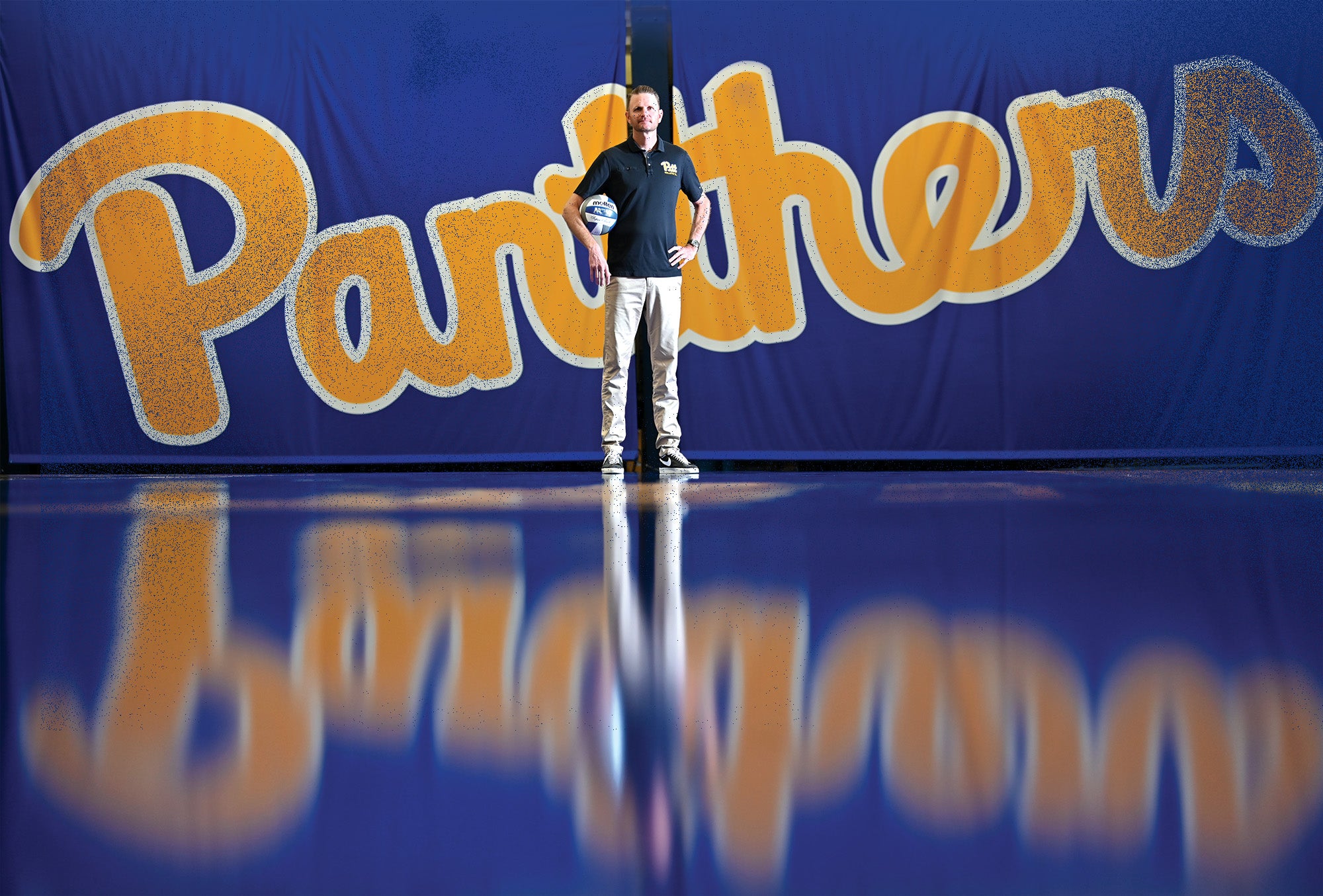 Fisher stands holding a volleyball in front of a Panthers logo