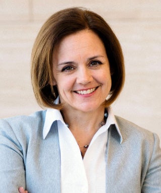 White woman with brown shoulder-length hair, baby blue blazer and white collared shirt smiles at camera