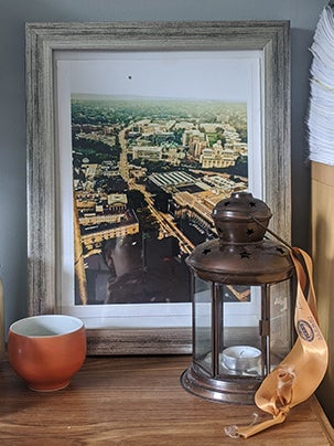 bronze-colored lantern with ribbon sitting in front of photo of Pitt campus