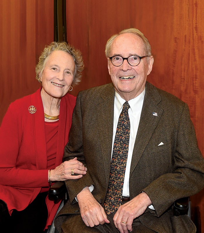 woman in red cardigan and blouse, man in brown suit sitting in wheelchair