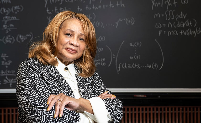 Elayne Arrington stands in front of a blackboard with math equations in white chalk