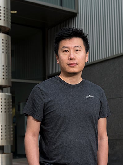 man wearing dark gray, short-sleeve t-shier stands and looks at camera