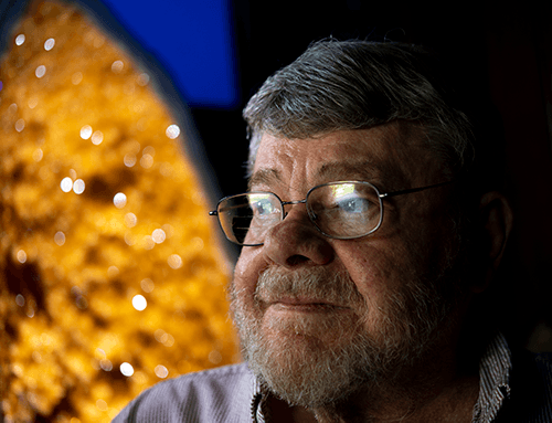 Older gentleman with glasses and salt-and-pepper hair, with giant, sparkling orange geode in background