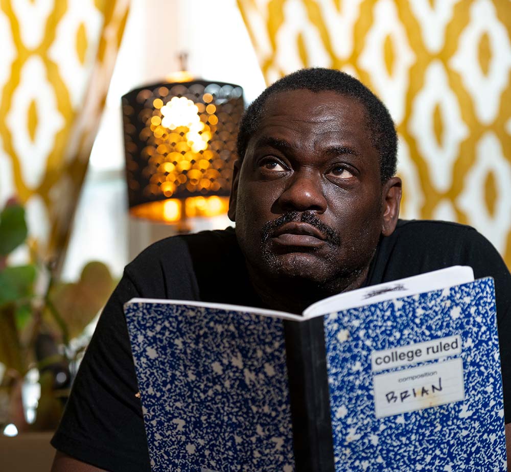 Black man holds up blue-marbled, college ruled composition book with "BRIAN" written in black on front