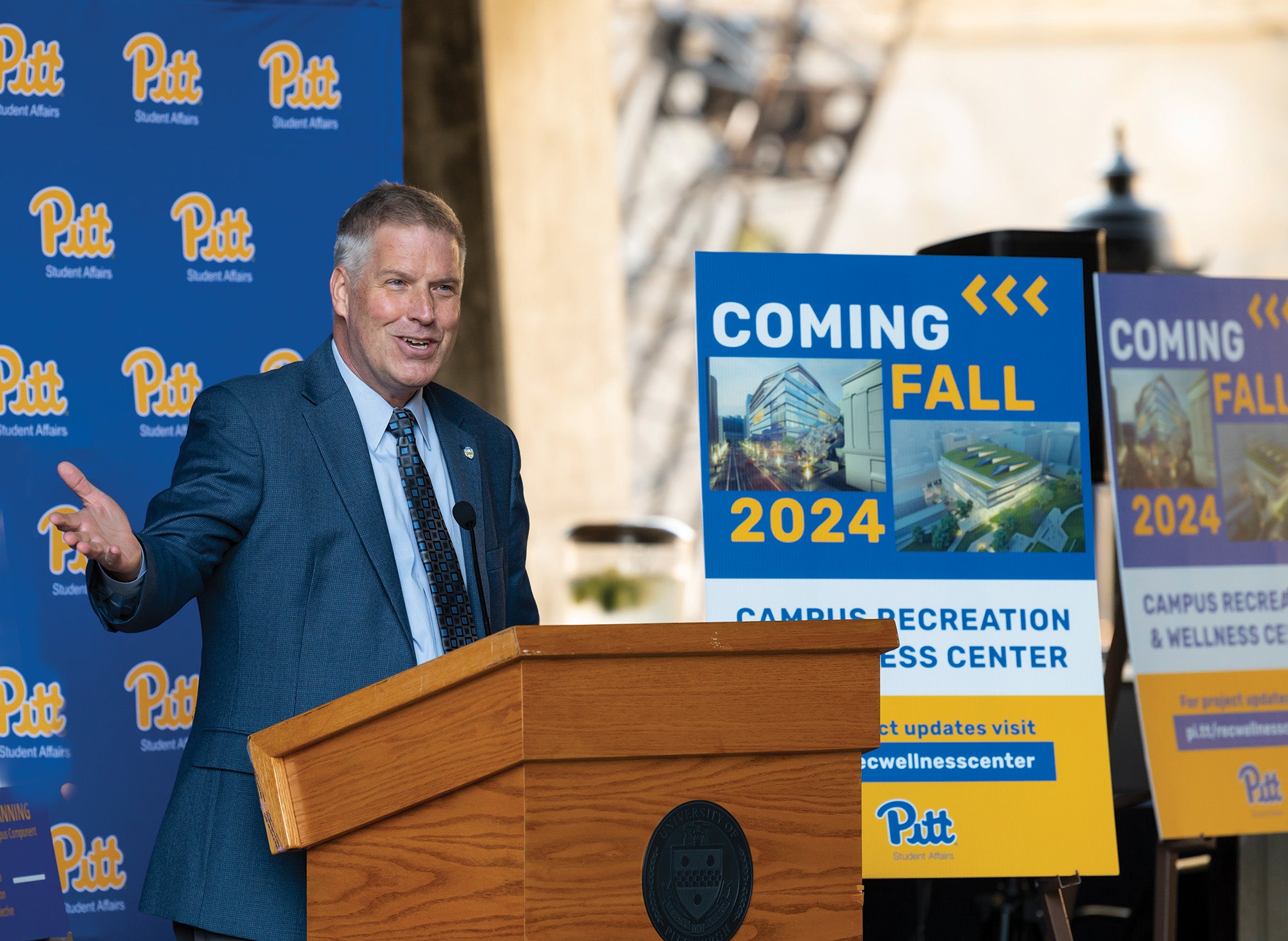 Gallagher speaks at a podium next to a sign advertising a new building