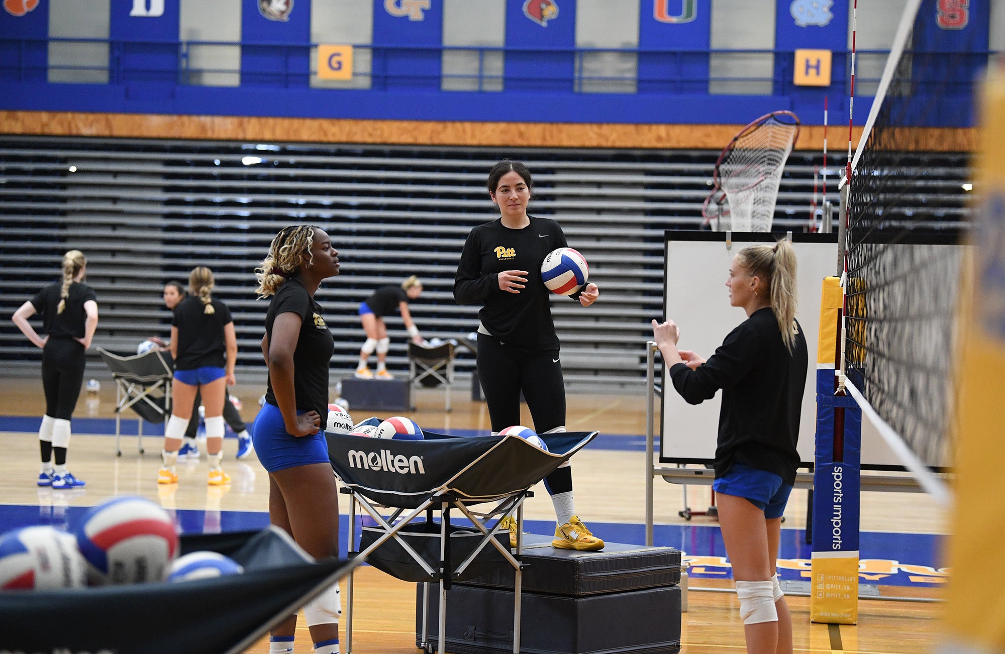 Three volleyball players talk on equipment in the gym