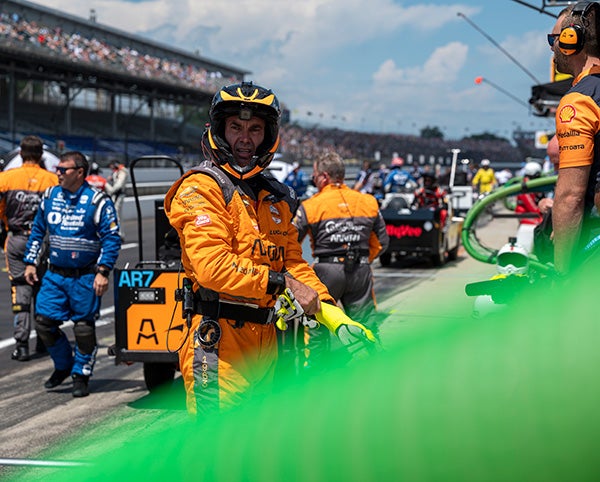O'Ward grimaces in an orange helmet and jumpsuit at a pit stop