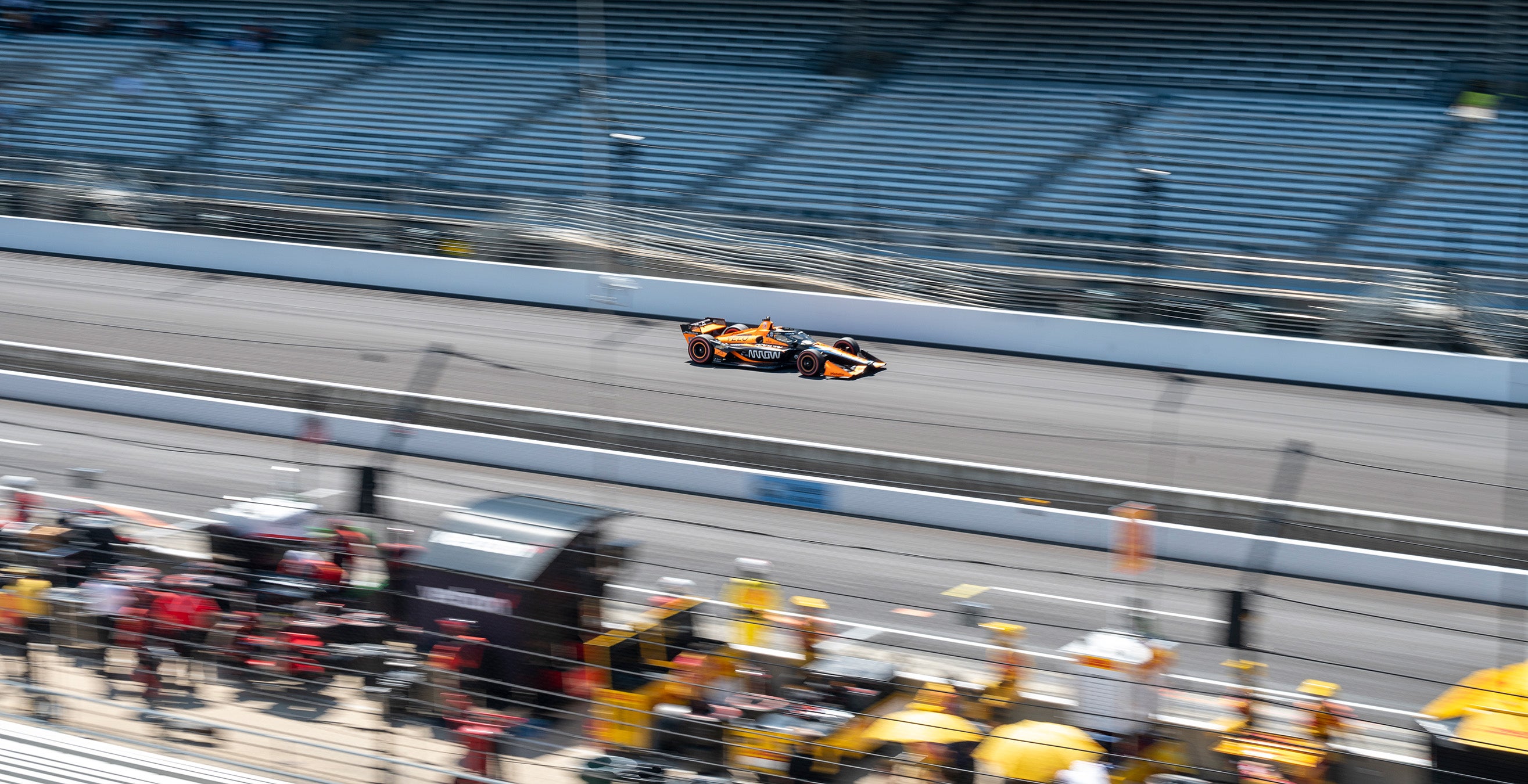Pitt crews and stands are blurred around the orange No. 5 IndyCar