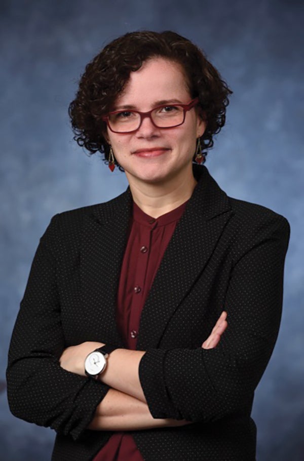 Carla Ng in black blazer and raspberry blouse, with matching glasses