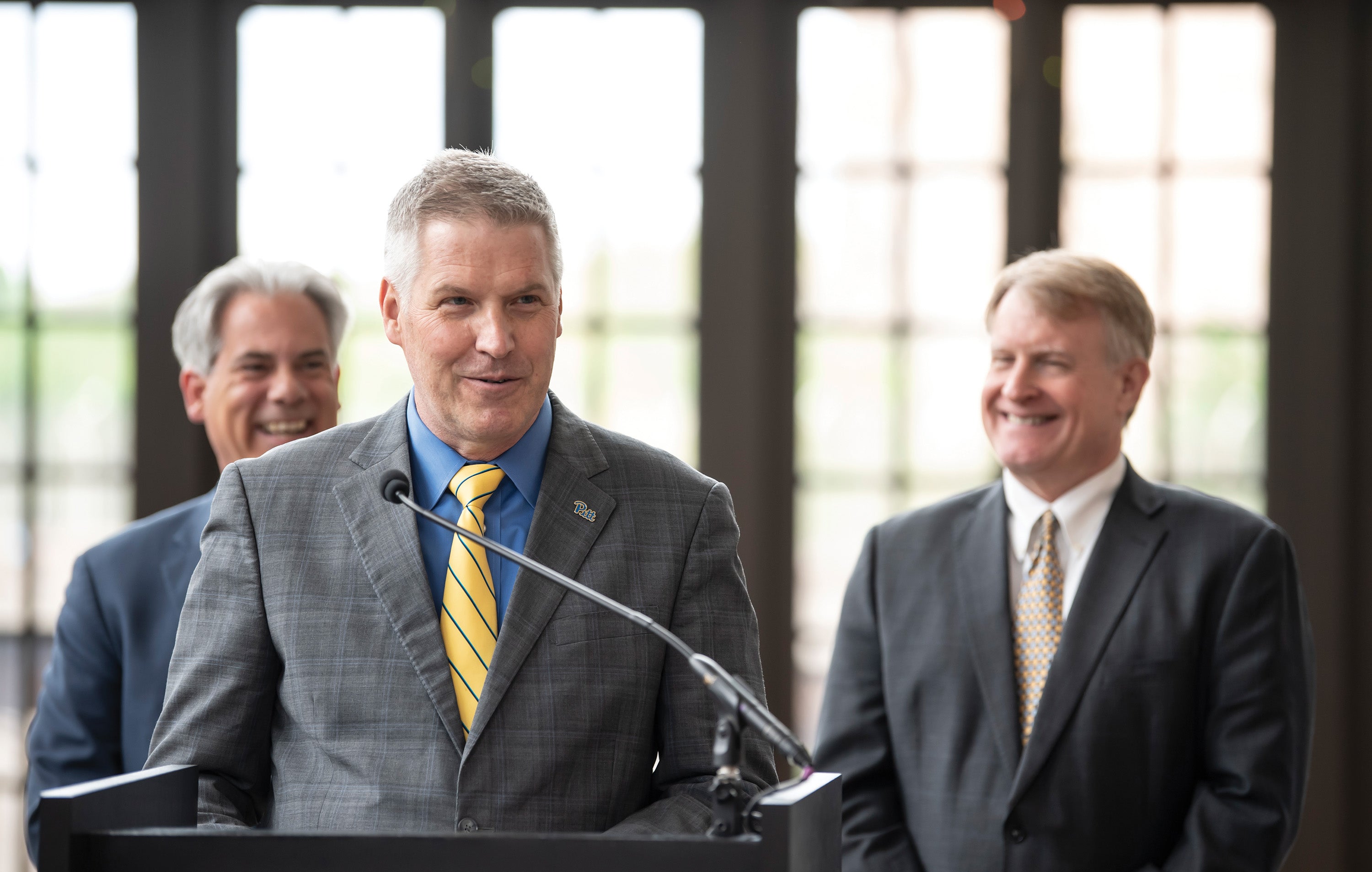 Gallagher speaks at a podium in a grey suit