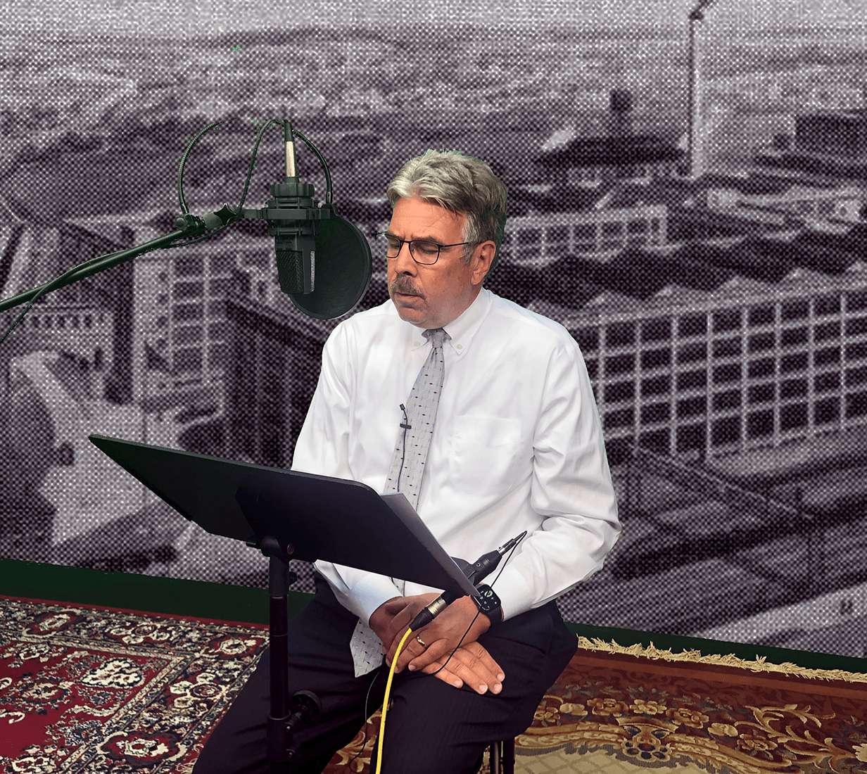 man with silver hair, mustache, wearing white button down and gray tie speaks into a recording microphone