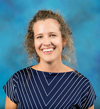 portrait of woman with curly light brown hair, wearing navy and white striped blouse, in front of teal background