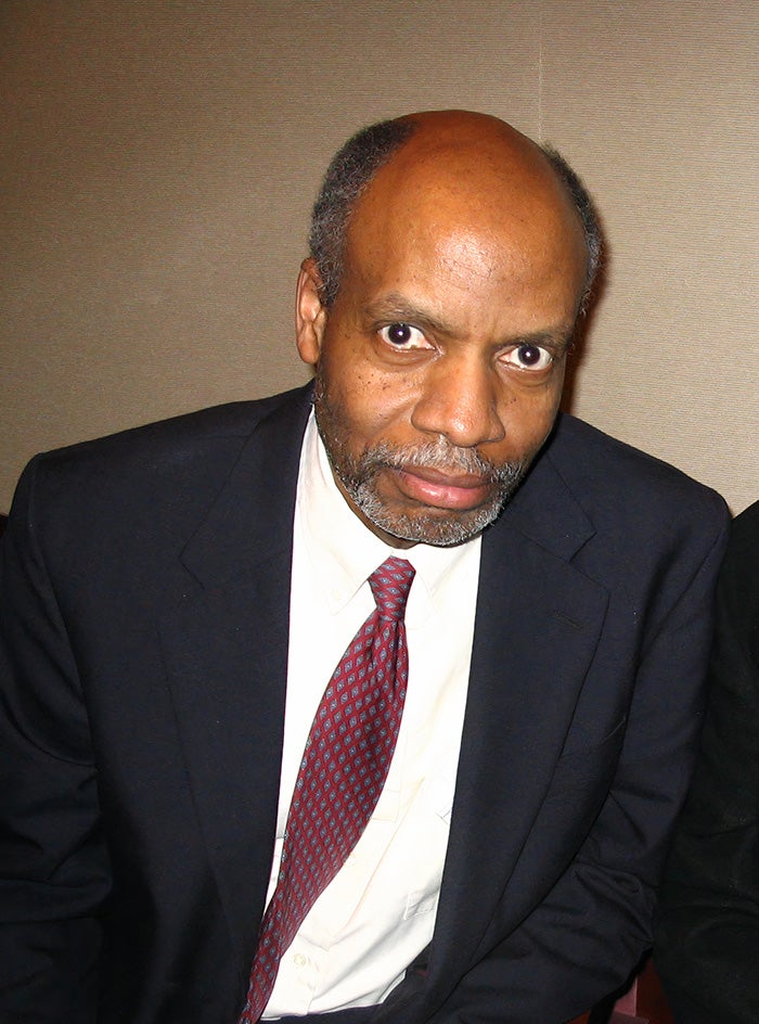 Mel Currie, man in dark suit, white-collared shirt and red tie, looks at camera