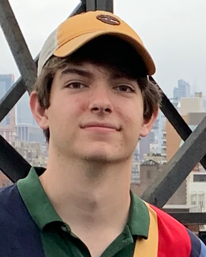 close-up photo of young main wearing multicolored polo, white and yellow baseball cap, with cityscape in background