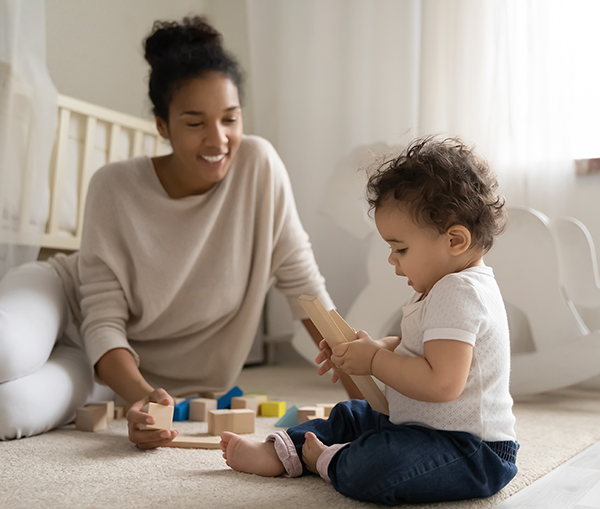 photo of black mother and mixed race baby sitting and playing with blocks on floor, muted colors on clothes and room decor