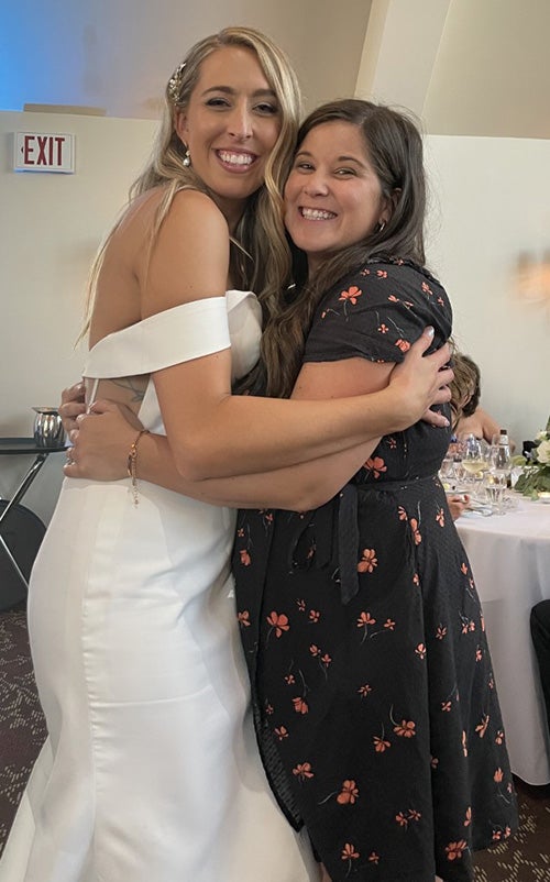 A person in a black dress hugs a person in a wedding dress