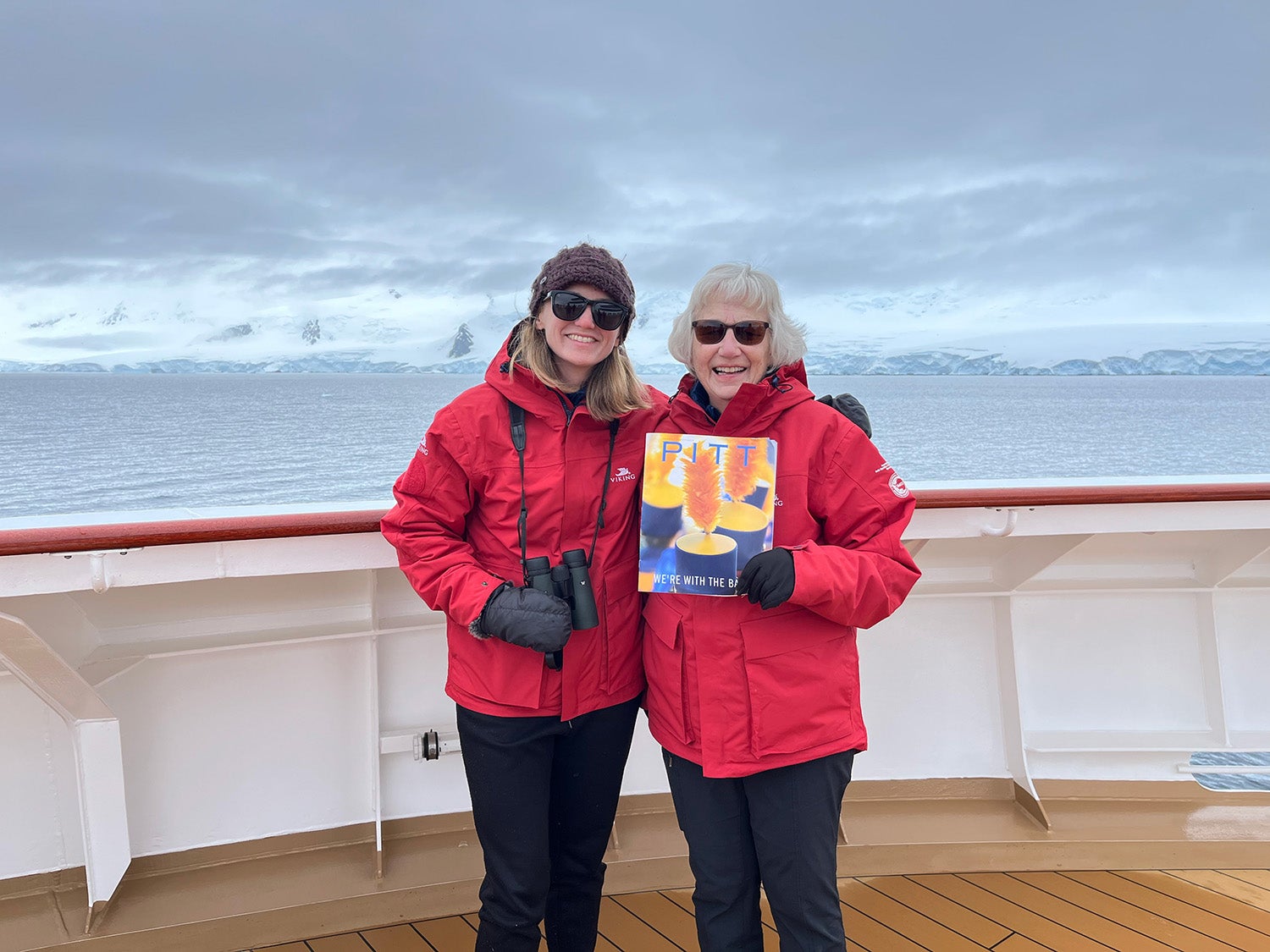 Two people in red jackets hold a magazine on a boat