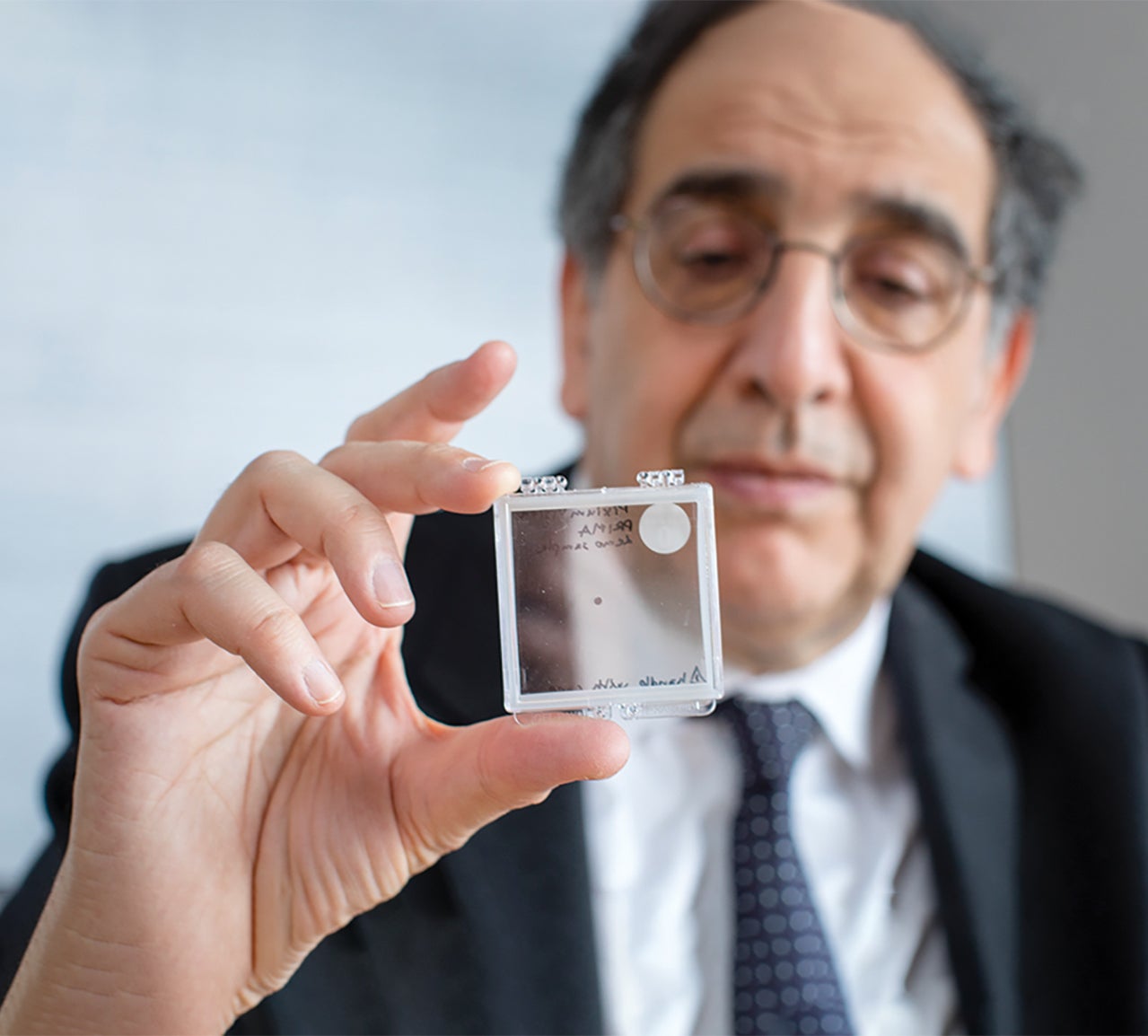 main in dark suit holds glass slide in focus for camera