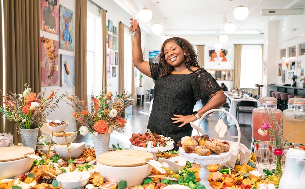 Thorne holds a glass above her head and a table of food