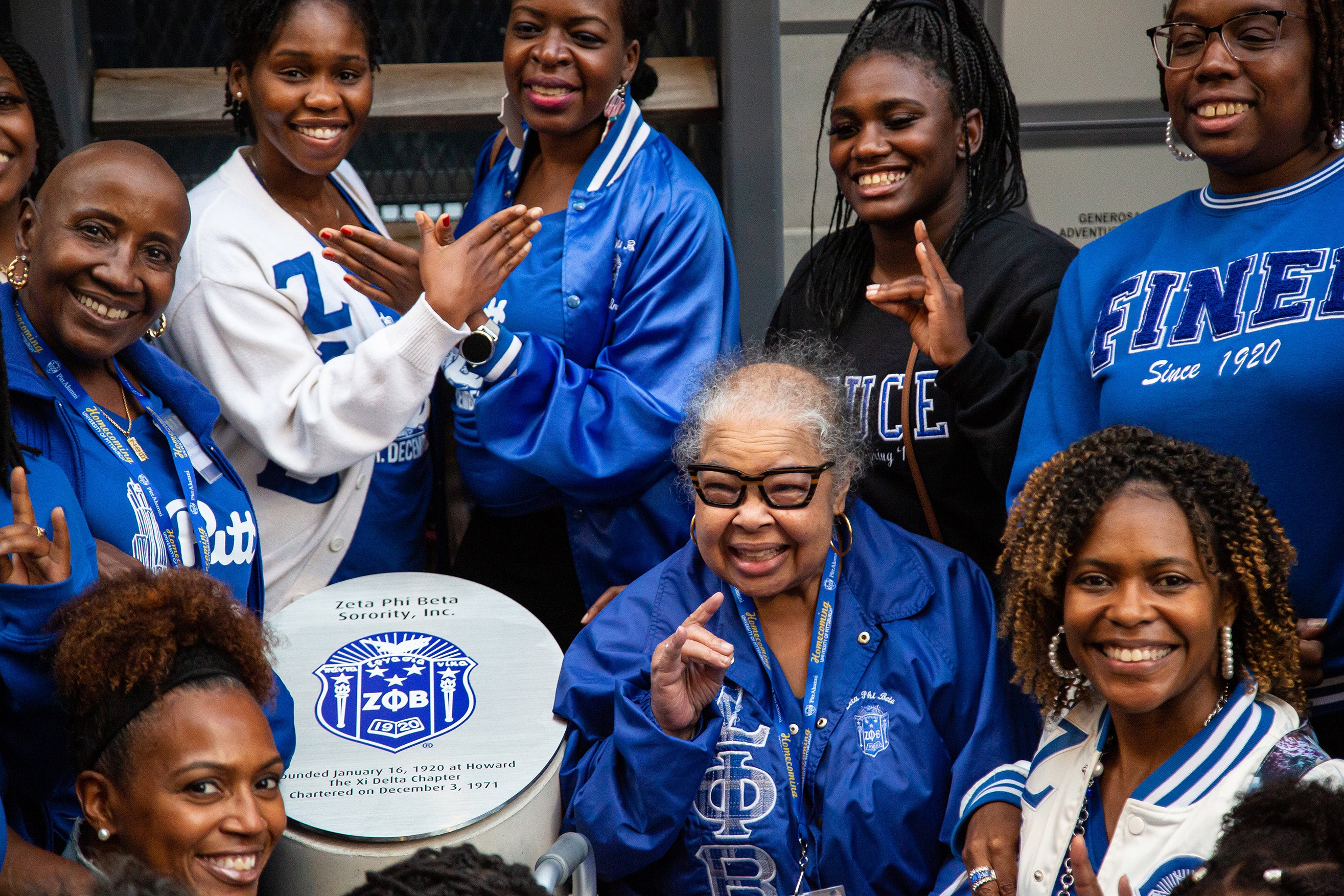 A group of Zeta Phi Beta sorority sisters wearing blue hold up hand symbols