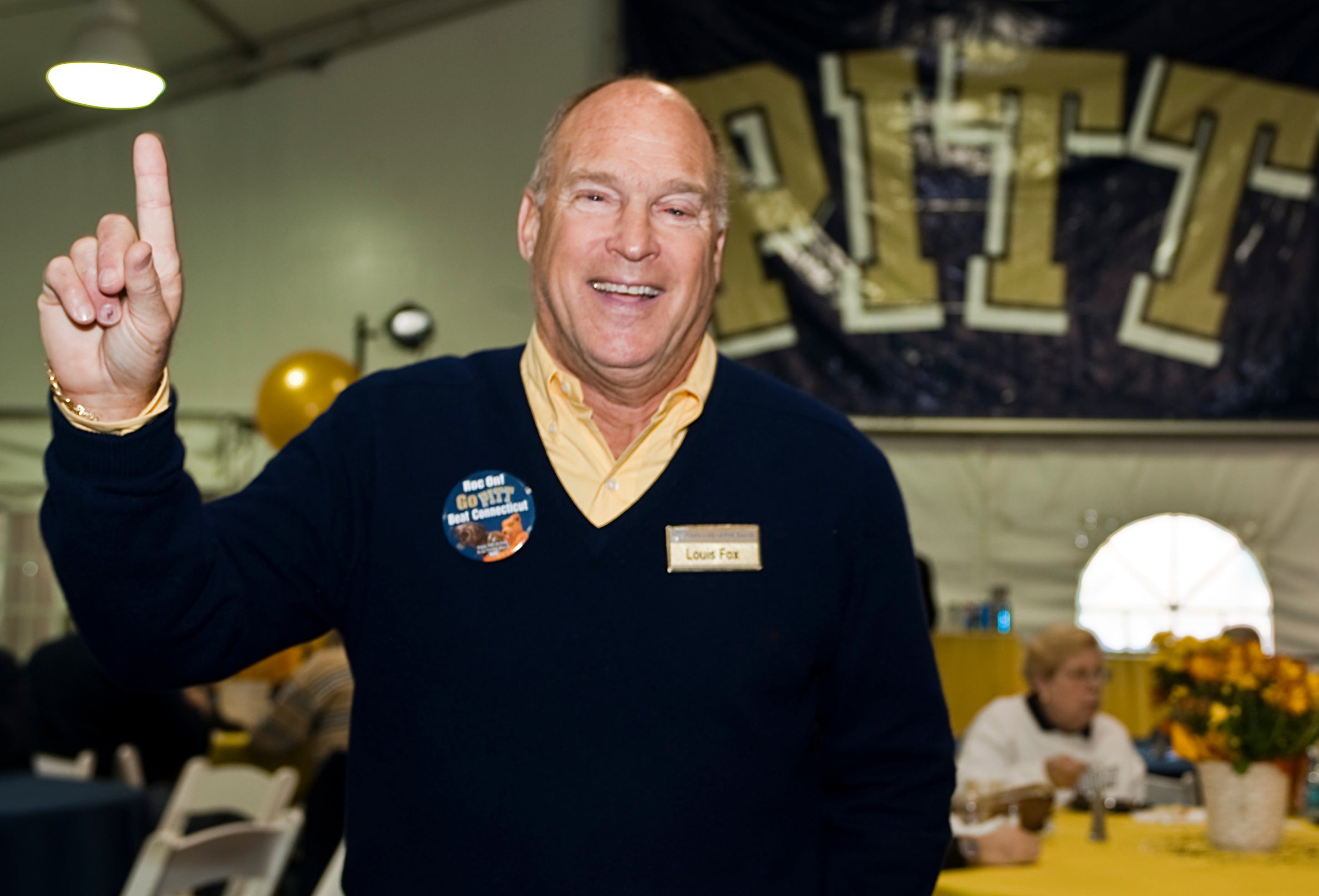 Louis J. Fox dressed in Pitt blue and gold, pointing his index finger toward the sky