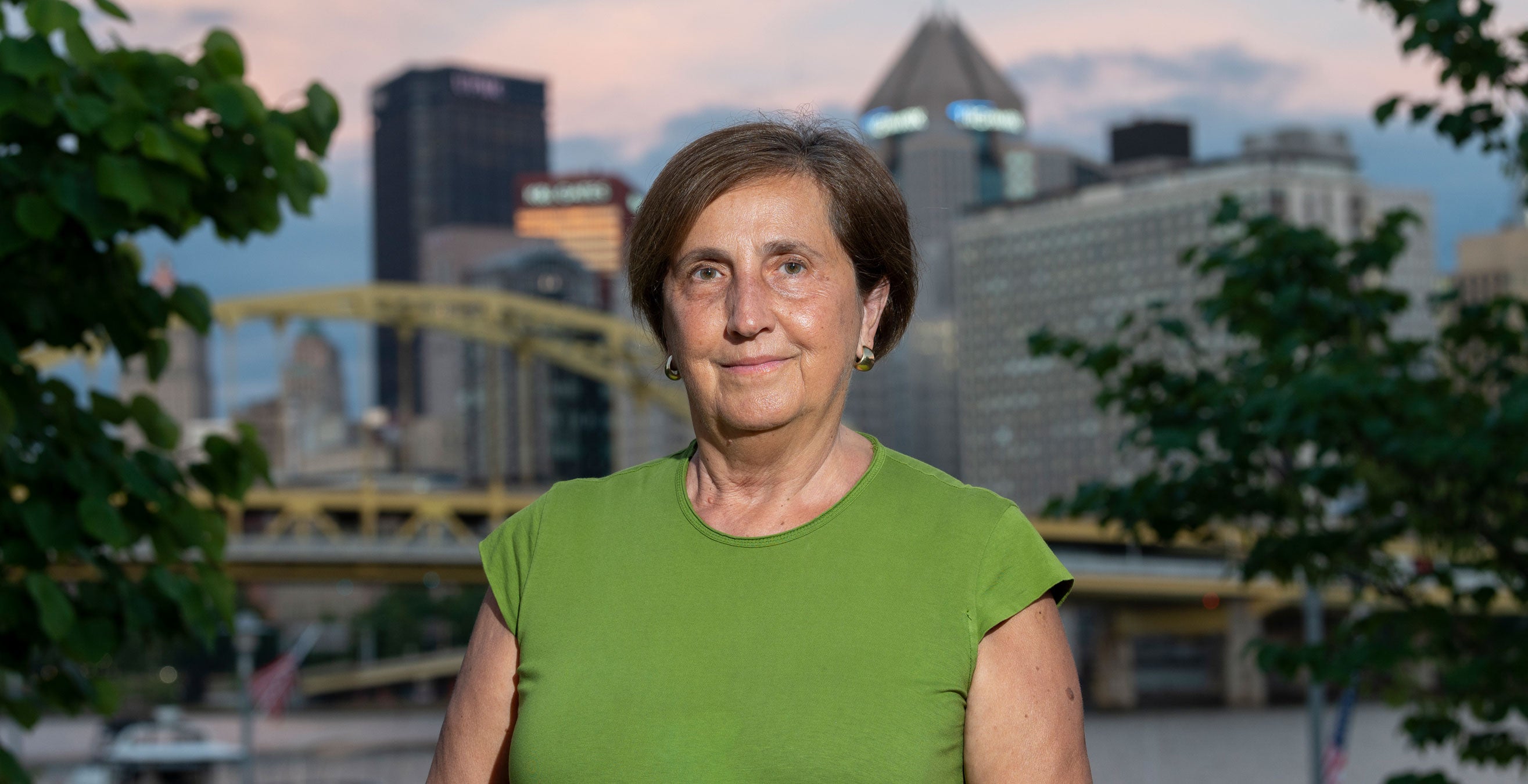 Olivera Finn wears a green shirt and stands before downtown Pittsburgh