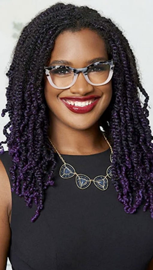 Young Back woman long, tightly curled hair, think-framedwhie and black glasses and black dress smiles at camera