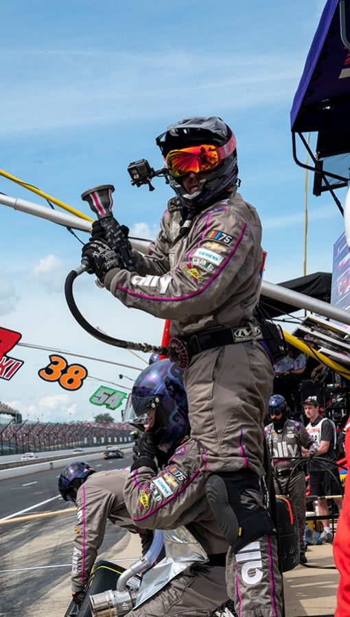 A pit crew member stands on a barrier in protective gear