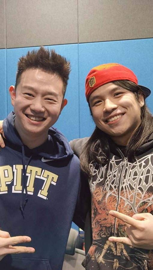 two young chinese men in sweatshirts stand in blue-walled sound booth