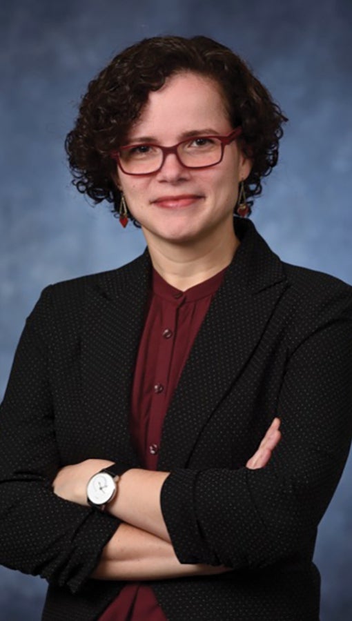 Carla Ng in black blazer and raspberry blouse, with matching glasses