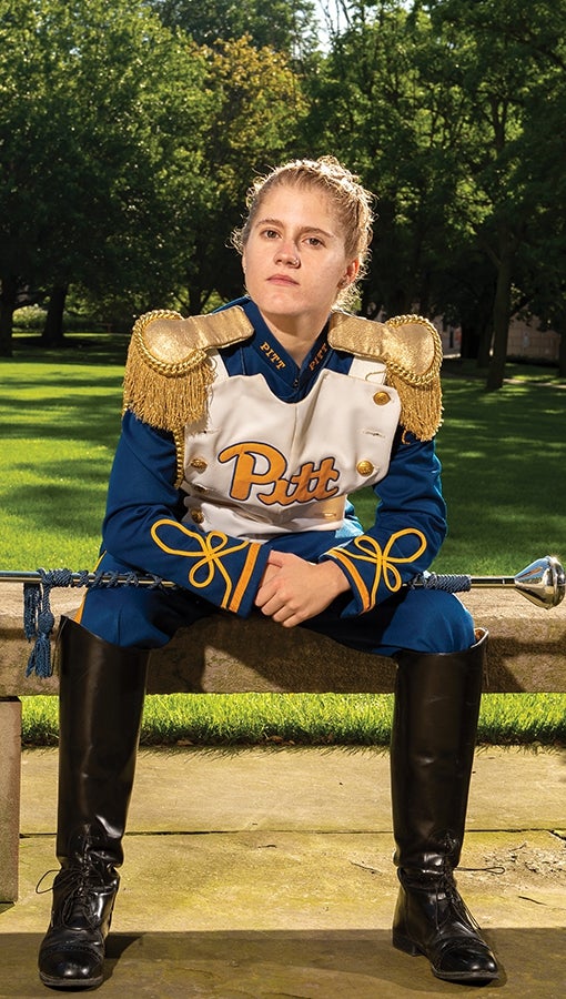 Pitt Band drum major Crissy Shannon sits in uniform in front of the Cathedral lawn.