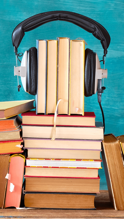 stacks of books, with over-the-ear headphones, on painted teal backdrop and wooden table