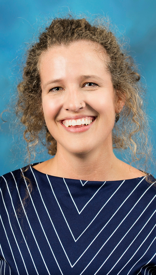 portrait of woman with curly light brown hair, wearing navy and white striped blouse, in front of teal background