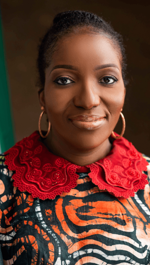 Head-shot of Black African woman wearing hair in bun, gold hoop earrings, top with red lace collar