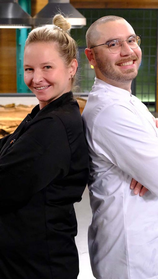 man and woman in chef coats back to back in studio kitchen