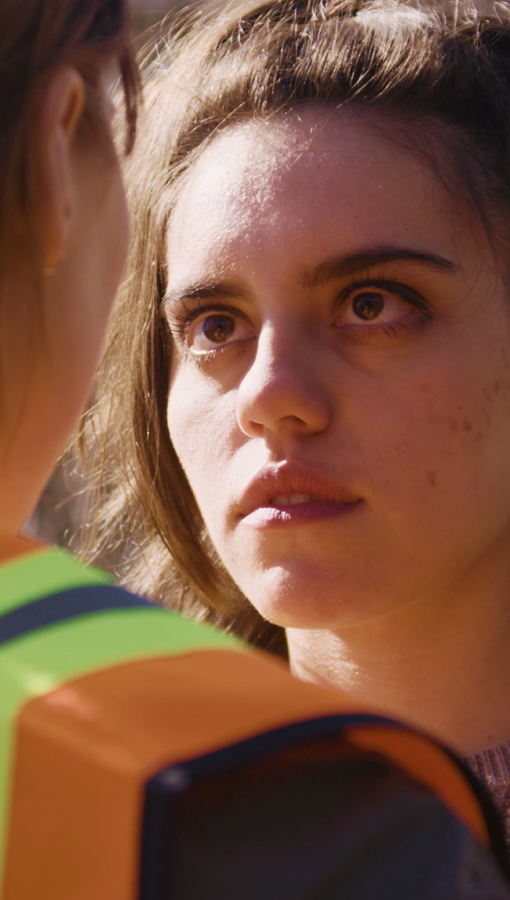 close up of young woman looking someone who is wearing orange safety vest in the eye while standing outside in the sun