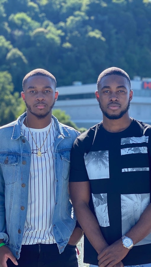 two young Black men stand in sunshine and look at camera