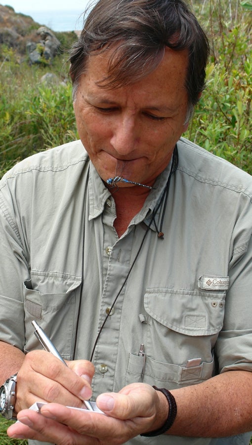 man with dragonfly specimen makes field notes