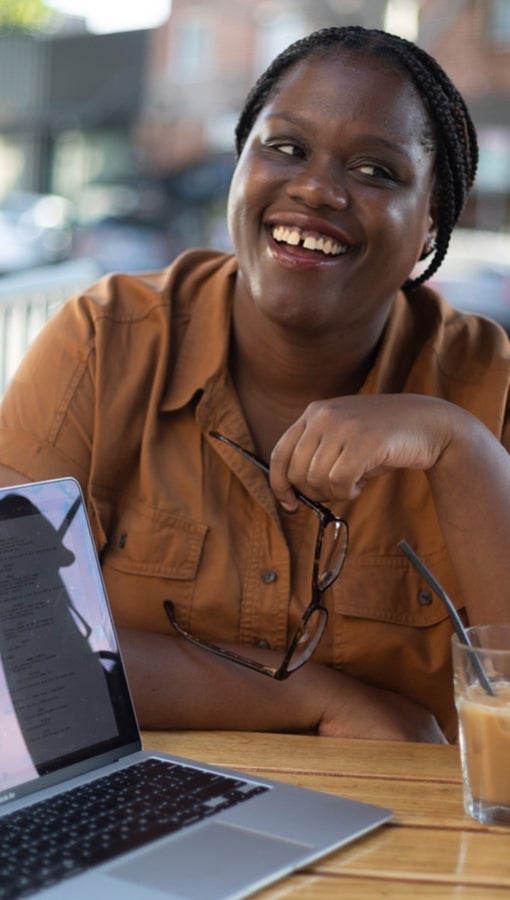 Kelechi Urama smiling with coffee and a laptop in front of her