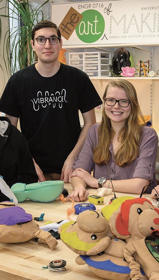 Jesse Rosenfeld and Caroline Westrick in the Art of Making studio, with backpack monkeys, electronics, fabric, spools of thread spread out on a table