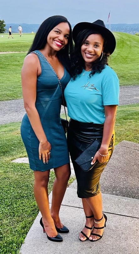 A person in a teal dress poses with a person in a black hat and teal shirt