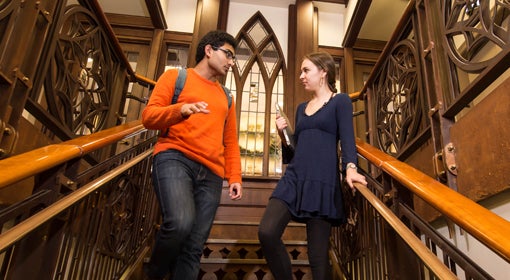 A man in an orange shirt talks to a woman in a blue dress while standing on a set of stairs