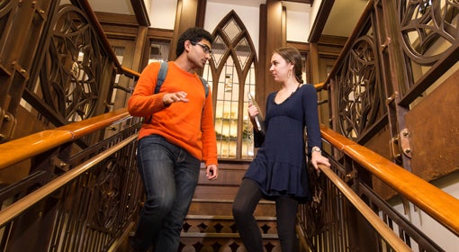 A man in an orange shirt talks to a woman in a blue dress while standing on a set of stairs