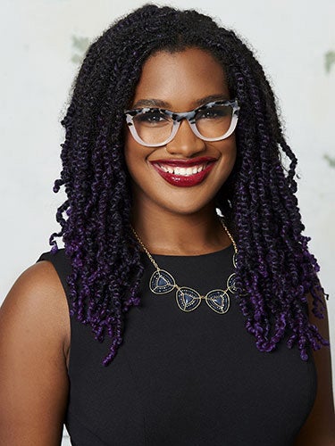 Young Back woman long, tightly curled hair, think-framedwhie and black glasses and black dress smiles at camera