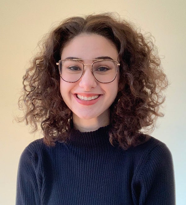 woman with shoulder-length curly brown hair and glasses wearing black turtleneck