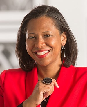 Black woman with straight brown shoulder length har and red blazer, black shirt and jewelry