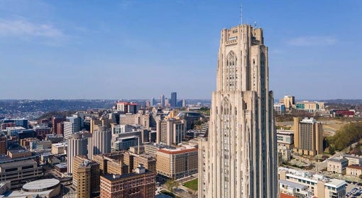 Drone-shot image of the Cathedral of Learning with Oakland and Downtown Pittsburgh in background