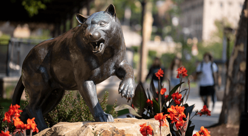 Panther statue with bright orange-red flowers, students walking in background