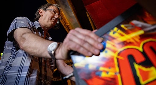 From below, Zumoff rests his hand on a pinball machine flipper button