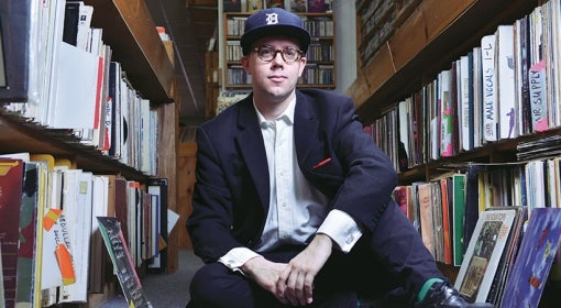 Carleton Gholz sitting between shelves of vinyl records.